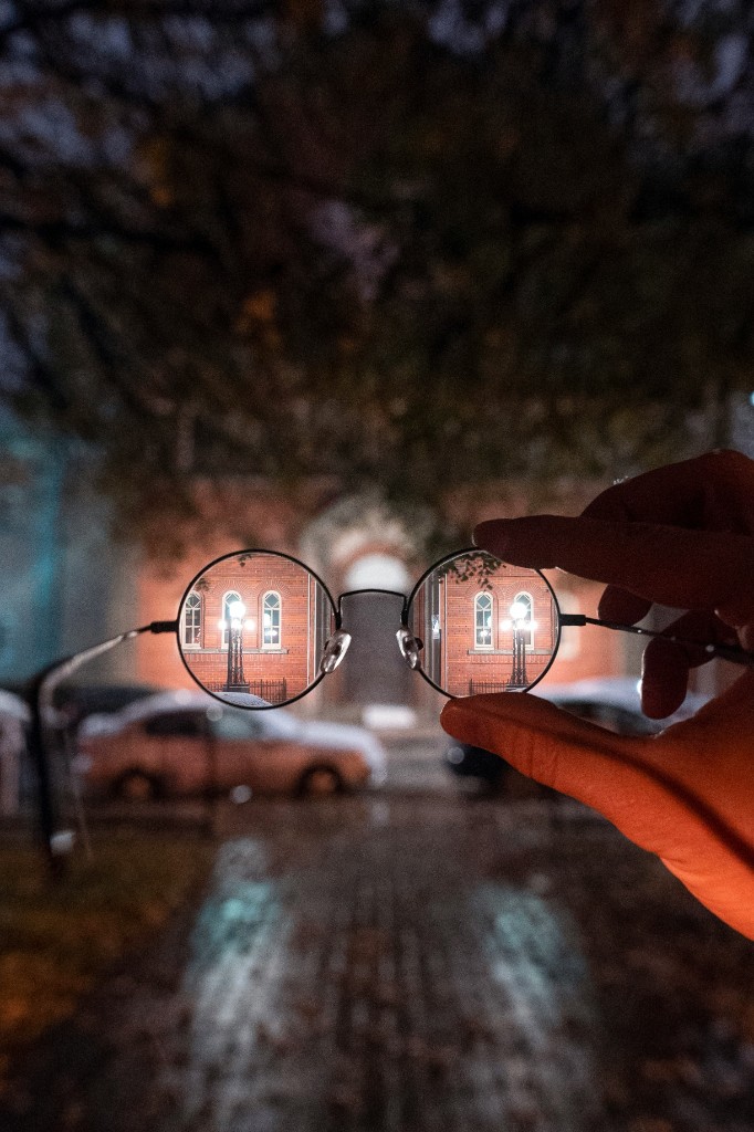 A hand holding round glasses that bring a blurred building into sharp focus — photo by Steven Wright on Unsplash